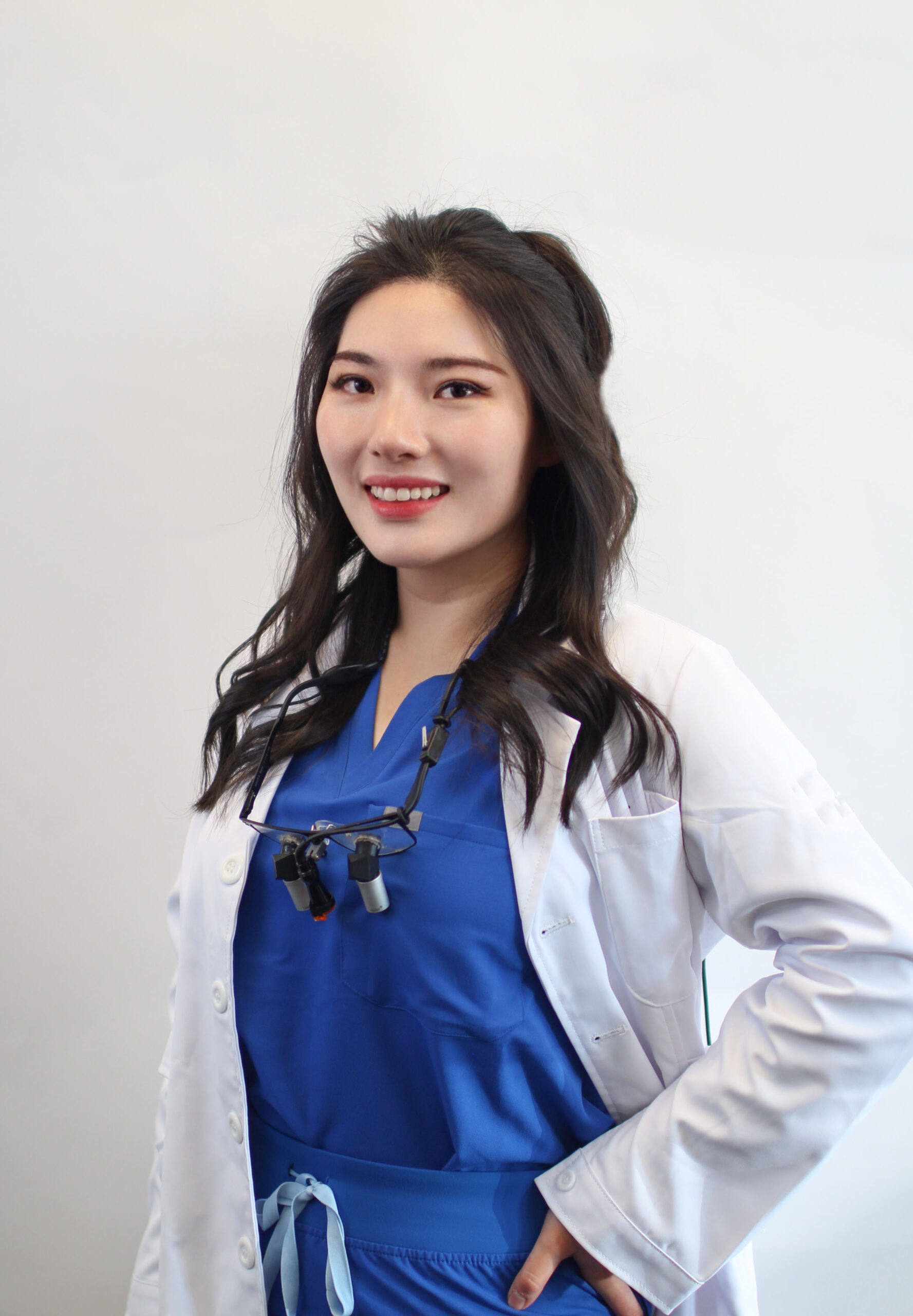 Su-Young Choi, DDS wearing magnifying loupes, seated in a well-lit office with plants in the background, smiling warmly - dentist federal way